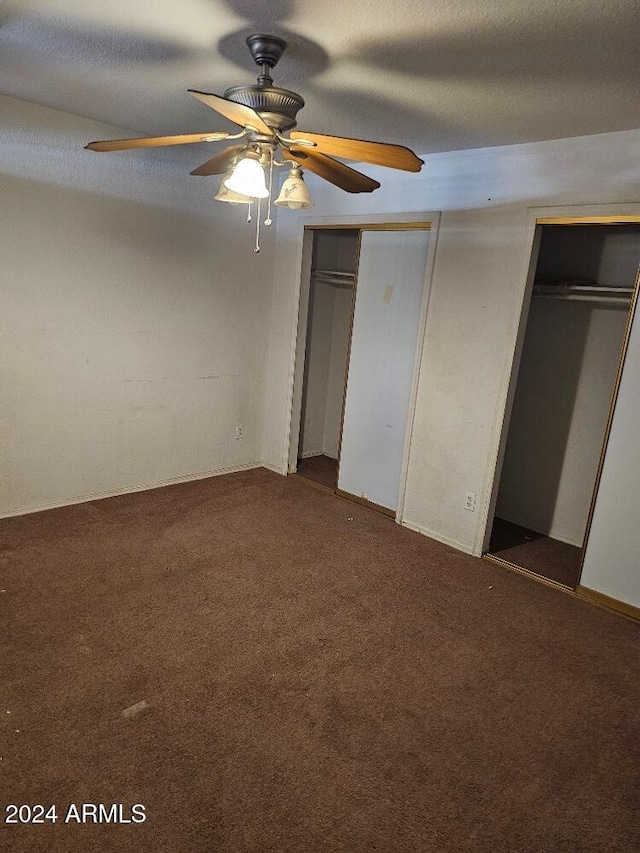 unfurnished bedroom with a textured ceiling, ceiling fan, carpet floors, and two closets