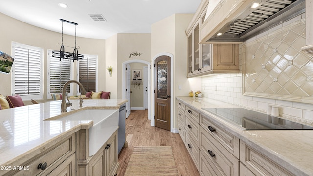 kitchen with arched walkways, black electric cooktop, premium range hood, visible vents, and tasteful backsplash