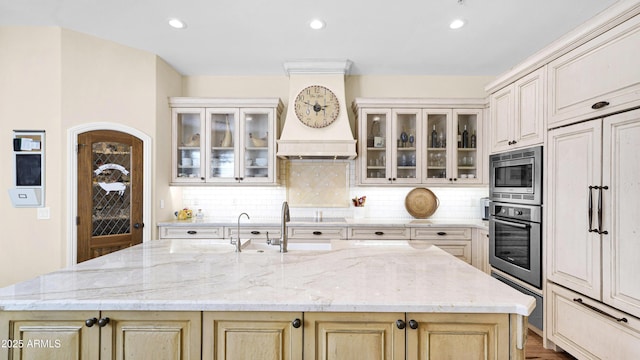 kitchen with an island with sink, light stone countertops, tasteful backsplash, and stainless steel appliances