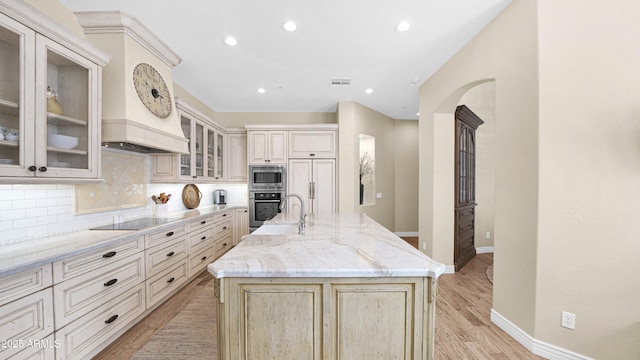 kitchen featuring visible vents, decorative backsplash, arched walkways, built in appliances, and light stone countertops