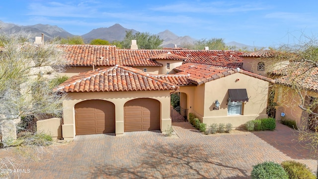 mediterranean / spanish-style home with a mountain view, a garage, a tiled roof, decorative driveway, and stucco siding