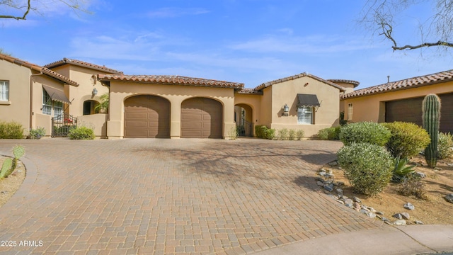 mediterranean / spanish house with a garage, a tiled roof, decorative driveway, and stucco siding