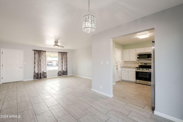 interior space with stainless steel appliances, decorative light fixtures, decorative backsplash, white cabinets, and ceiling fan with notable chandelier