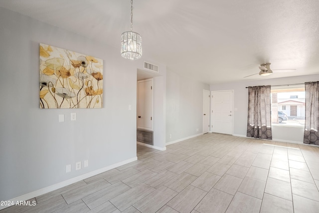 spare room featuring ceiling fan with notable chandelier