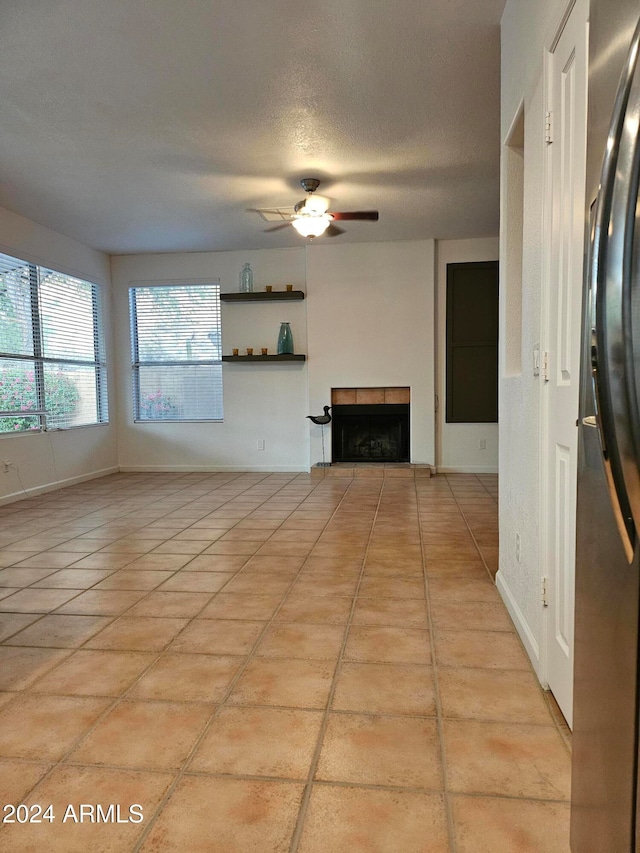 unfurnished living room featuring a textured ceiling, light tile patterned floors, ceiling fan, and a fireplace