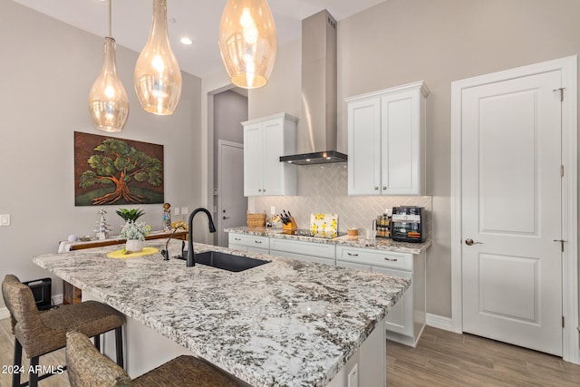 kitchen featuring tasteful backsplash, an island with sink, sink, and wall chimney exhaust hood