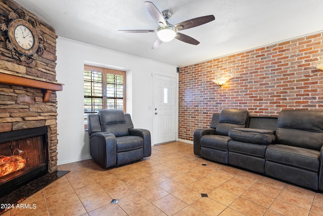 living room with ceiling fan, light tile patterned flooring, brick wall, a textured ceiling, and a fireplace