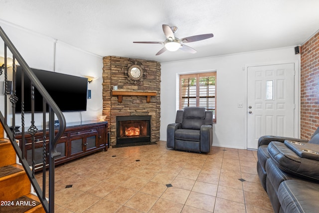 living room with light tile patterned flooring, ceiling fan, a stone fireplace, ornamental molding, and a textured ceiling