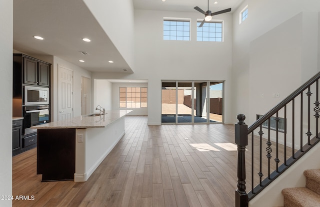 kitchen featuring sink, an island with sink, stainless steel appliances, a high ceiling, and light hardwood / wood-style flooring