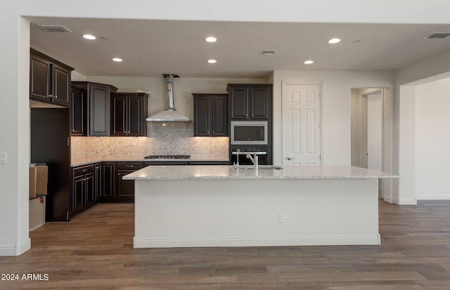 kitchen with wall chimney exhaust hood, hardwood / wood-style floors, a kitchen island with sink, and sink