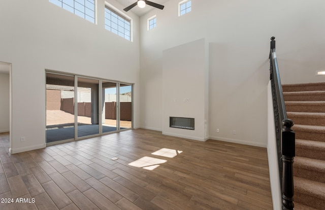 unfurnished living room featuring a towering ceiling, hardwood / wood-style floors, and ceiling fan