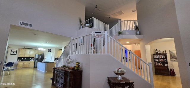staircase featuring arched walkways, wood finished floors, a towering ceiling, and visible vents