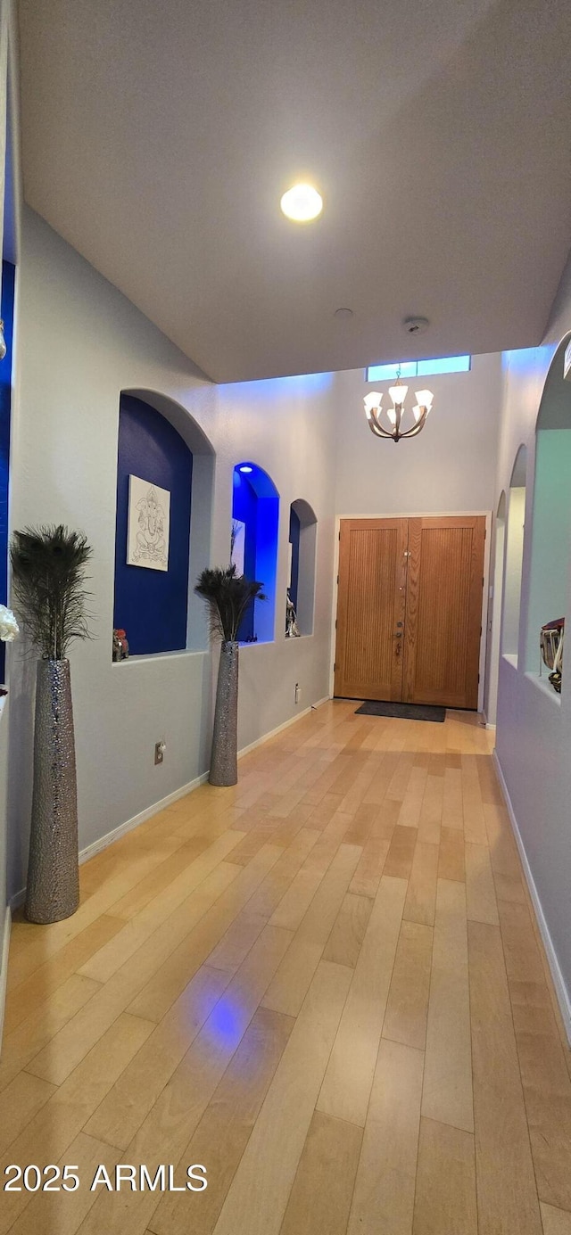 hall featuring a chandelier, arched walkways, and baseboards