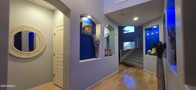 hall with arched walkways, baseboards, a high ceiling, wood finished floors, and stairway