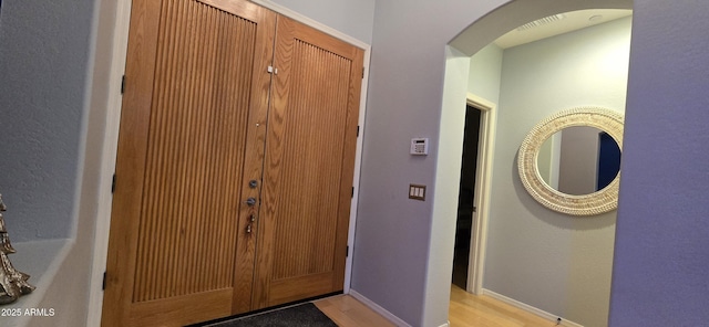 foyer featuring light wood-type flooring, baseboards, and arched walkways