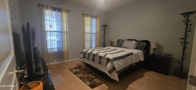 bedroom featuring wood finished floors, lofted ceiling, baseboards, and multiple windows