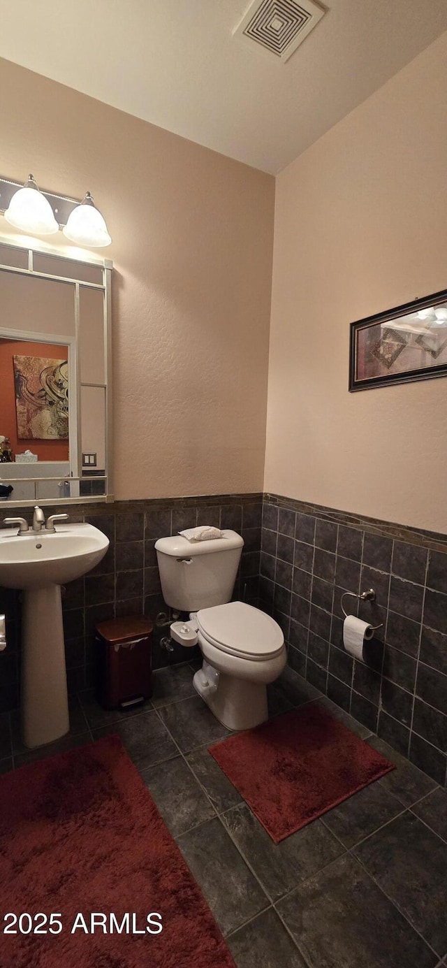 half bathroom with wainscoting, tile patterned flooring, visible vents, and tile walls