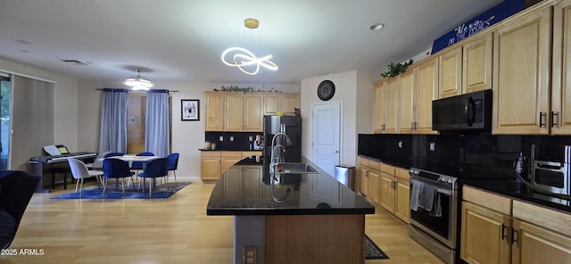 kitchen with light brown cabinetry, dark countertops, a sink, tasteful backsplash, and appliances with stainless steel finishes