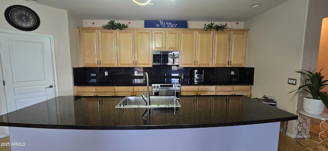 kitchen featuring a sink, stainless steel microwave, dark countertops, decorative backsplash, and light brown cabinets