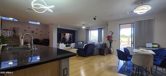 kitchen with light wood finished floors, a sink, open floor plan, dark countertops, and visible vents