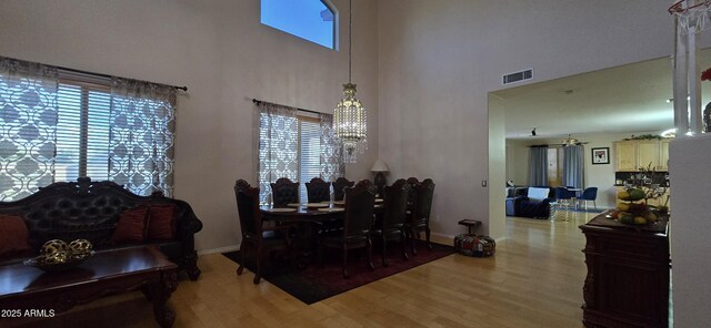 dining space featuring a towering ceiling, visible vents, baseboards, ceiling fan with notable chandelier, and wood finished floors
