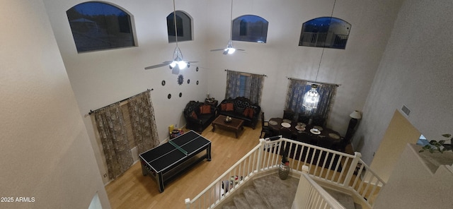 interior space with a towering ceiling, a ceiling fan, and wood finished floors