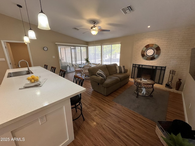 living area featuring a brick fireplace, visible vents, vaulted ceiling, and wood finished floors