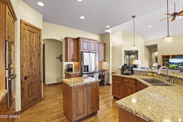 kitchen with sink, appliances with stainless steel finishes, a center island, light stone counters, and decorative light fixtures