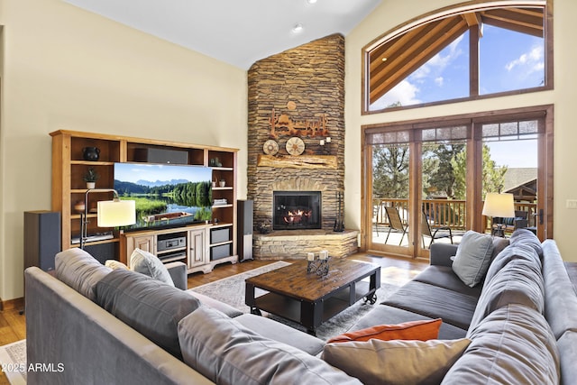 living room with high vaulted ceiling, a stone fireplace, and light hardwood / wood-style floors