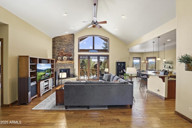 living room with a stone fireplace, ceiling fan with notable chandelier, high vaulted ceiling, and dark hardwood / wood-style floors