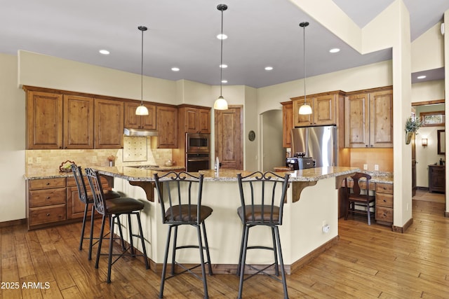 kitchen featuring a large island, stainless steel appliances, light stone counters, a kitchen bar, and decorative light fixtures