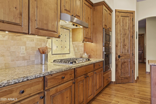 kitchen with light stone counters, stainless steel appliances, light hardwood / wood-style floors, and tasteful backsplash