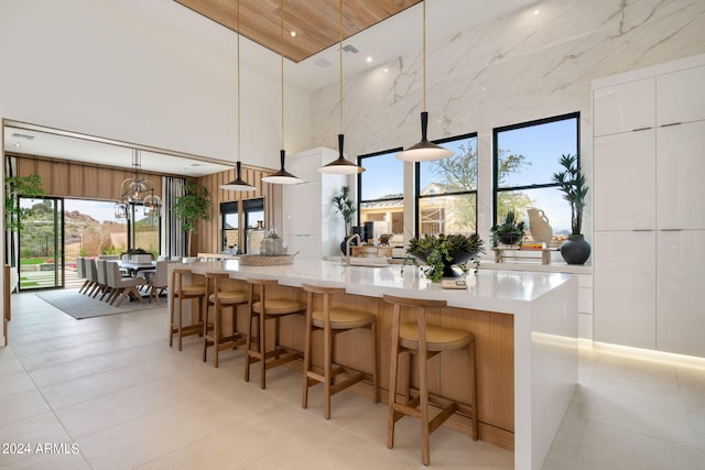 kitchen with a towering ceiling, a breakfast bar, white cabinetry, hanging light fixtures, and a large island