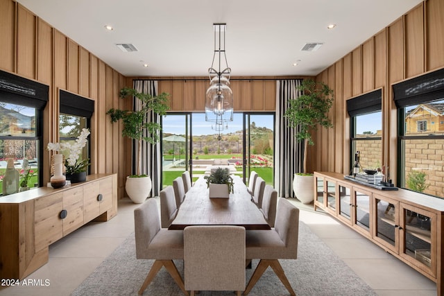 dining space featuring a notable chandelier, light tile patterned flooring, and wooden walls