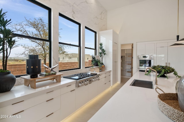 kitchen featuring white cabinets, high vaulted ceiling, stainless steel gas stovetop, and sink