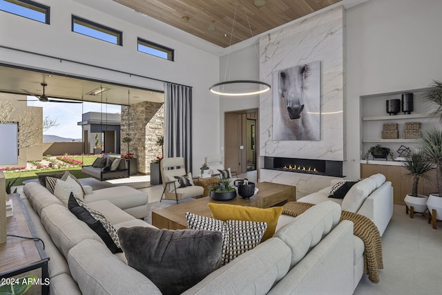 tiled living room featuring wooden ceiling, ceiling fan, a premium fireplace, a towering ceiling, and built in features