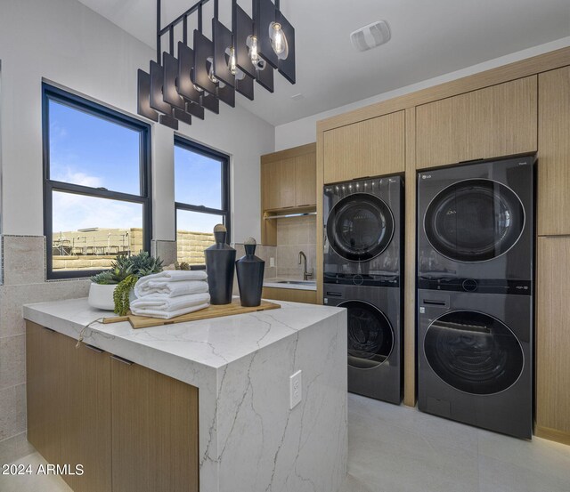 laundry room featuring cabinets, stacked washing maching and dryer, and sink