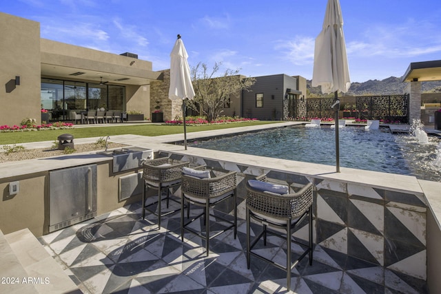 view of pool with pool water feature, ceiling fan, exterior kitchen, and a patio