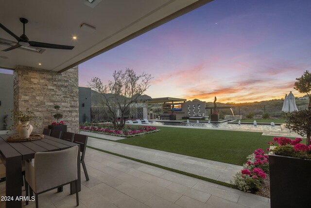 patio terrace at dusk featuring a yard and ceiling fan