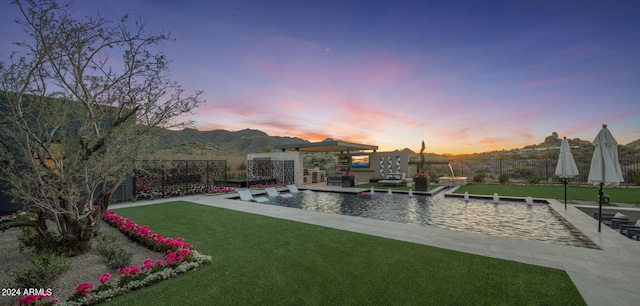 pool at dusk featuring a mountain view, a yard, and pool water feature