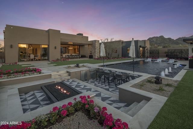 pool at dusk with a mountain view, a patio, an outdoor bar, and an outdoor fire pit