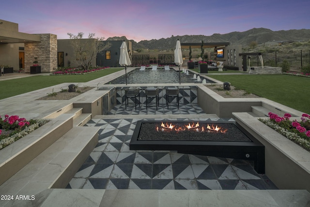 pool at dusk featuring a lawn, a patio area, a mountain view, and an outdoor bar