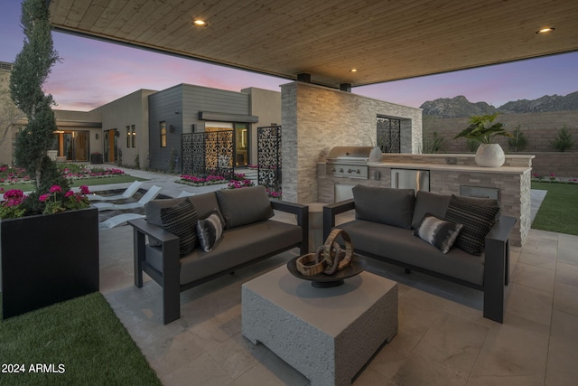 patio terrace at dusk featuring an outdoor living space, area for grilling, and exterior kitchen