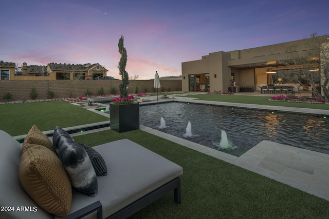 pool at dusk with pool water feature and a yard