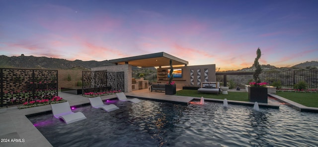 pool at dusk with pool water feature, an outdoor living space, and a mountain view