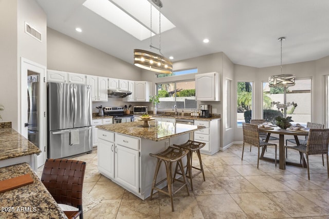 kitchen with pendant lighting, a skylight, stainless steel appliances, a center island, and white cabinets