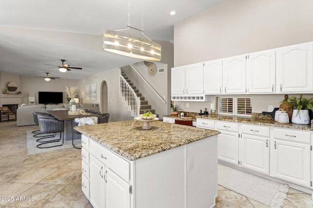 kitchen with hanging light fixtures, white cabinetry, a center island, and light stone counters