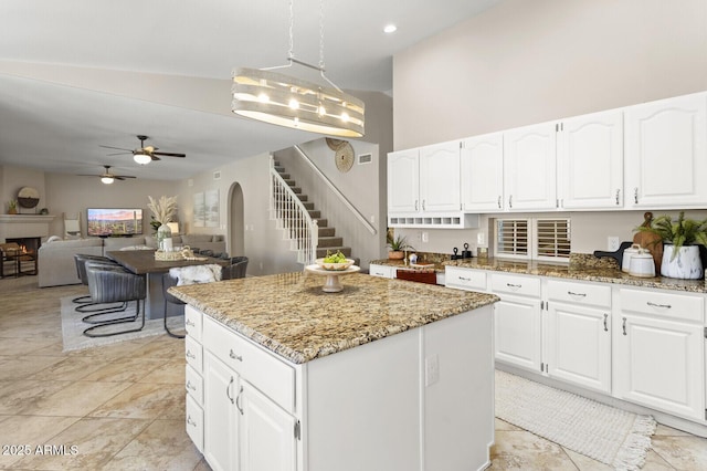 kitchen with a center island, pendant lighting, ceiling fan, light stone countertops, and white cabinets