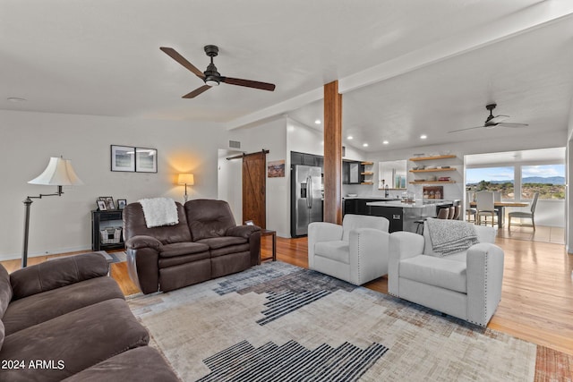 living room with light hardwood / wood-style flooring, vaulted ceiling with beams, ceiling fan, and a barn door