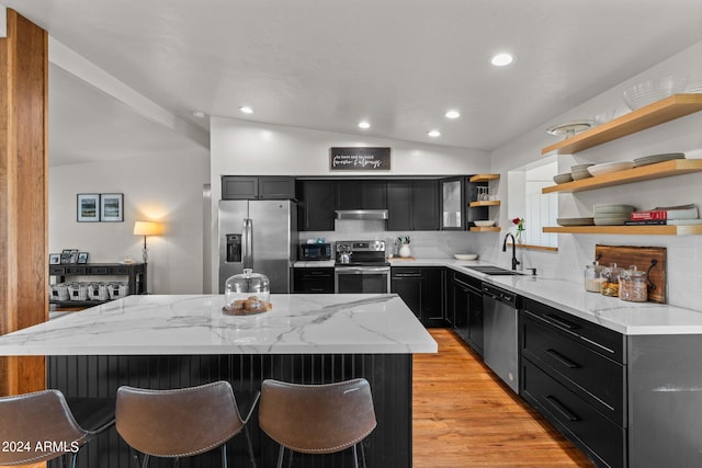 kitchen with sink, appliances with stainless steel finishes, a center island, light stone countertops, and vaulted ceiling